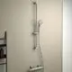 Brausethermostat von Ideal Standard, montiert an einer Wand, mit einer Brausestange und einem Handbrausekopf, hinter einem Regalelement.